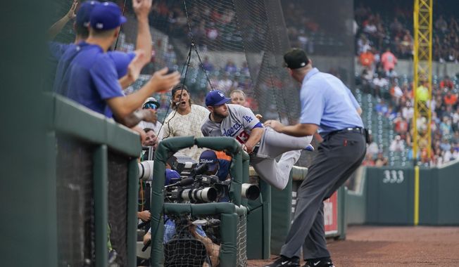 Los Angeles Dodgers third baseman Max Muncy, center, leans over the railing in the photographers pit while making a catch on a foul ball by Baltimore Orioles&#x27; Adley Rutschman during the second inning of a baseball game, Monday, July 17, 2023, in Baltimore. Third base umpire Nate Tomlinson, right, looks on. (AP Photo/Julio Cortez)