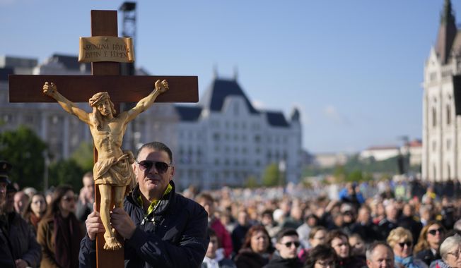 A man holds a crucifix as he waits for Pope Francis arrival for a mass in Kossuth Lajos Square in Budapest, Hungary, Sunday, April 30, 2023.. (AP Photo/Andrew Medichini)