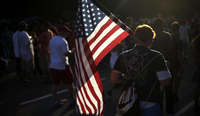 FILE - A young man walks with an American flag at an Independence Day celebration on the Benjamin Franklin Parkway, July 4, 2013, in Philadelphia. Flags proliferate every July Fourth, but unlike the right to assemble or trial by jury, their role was not prescribed by the founders: They would have been rare during early Independence Day celebrations. (AP Photo/Matt Rourke, File)